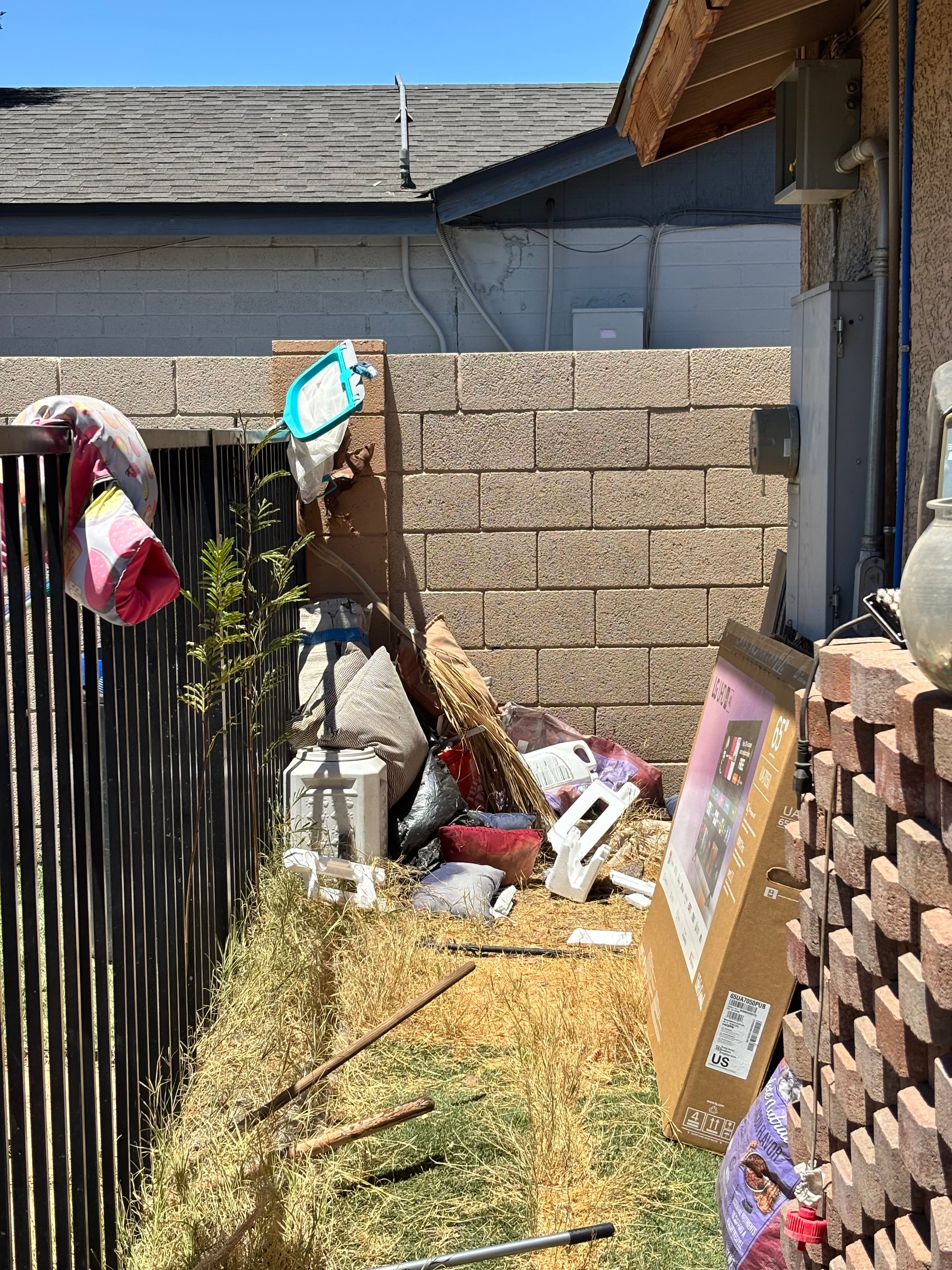 Cluttered backyard with trash bags, a large TV box, and debris against a block wall.