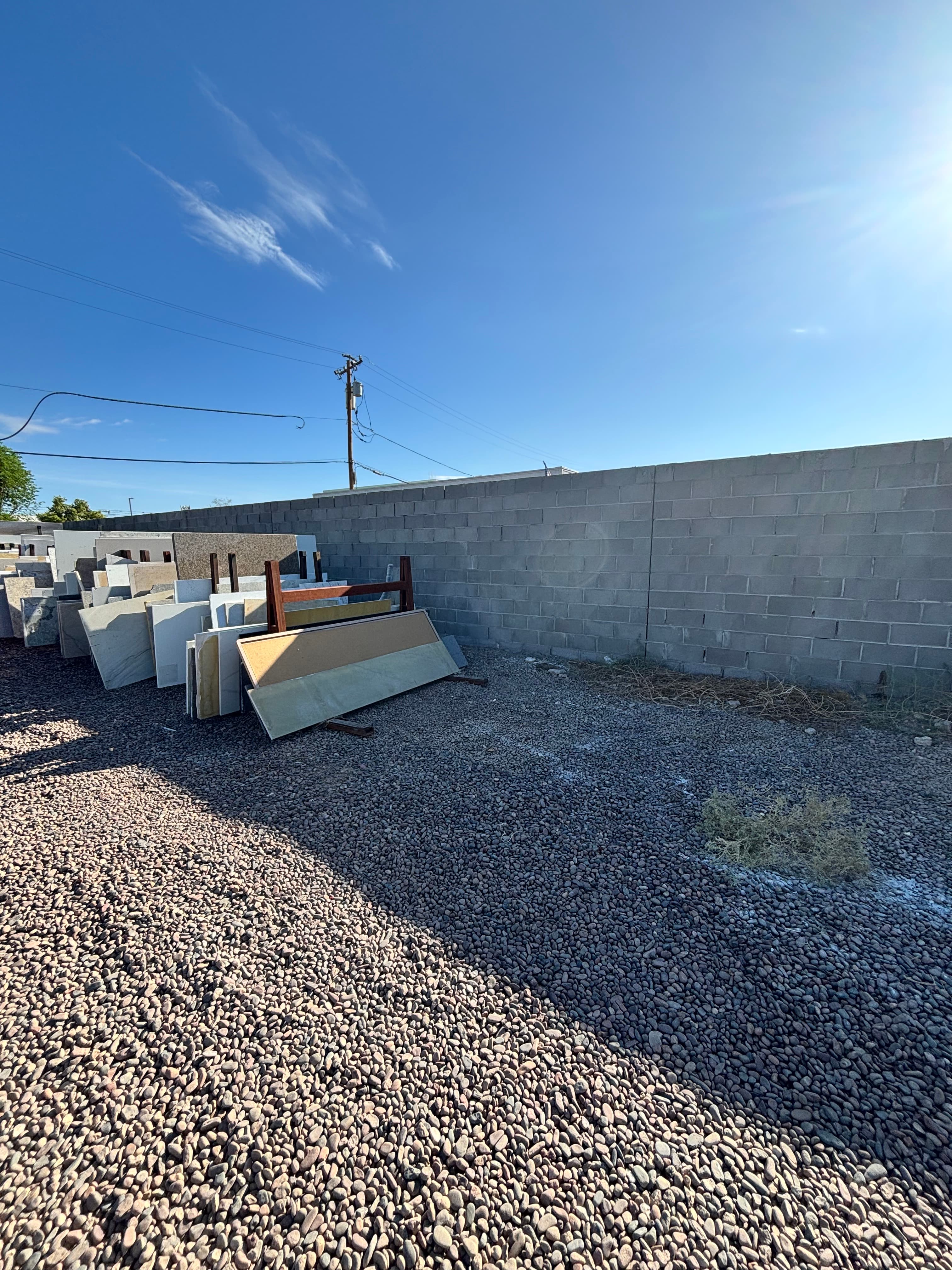 Stone slabs leaning against a rack in a gravel yard under a bright blue sky.